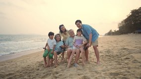 4K Group of Multi-Generation Asian family travel ocean on summer holiday vacation. Happy big family having fun outdoor lifestyle using mobile phone taking selfie together at tropical beach in sunset.