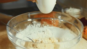 Mixing fresh eggs with steel hand mixer in a glass bowl. Adding flour. Process of preparing pancakes. 4K video