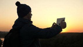 Traveler man travels with digital tablet in natural park. Hiker takes pictures on tablet computer from top of mountain against backdrop of beautiful landscape. Modern technologies. Outdoor traveler