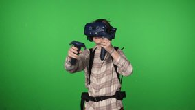 An emotional teenage boy in virtual reality equipment is playing a video game on a green background. VR glasses. Chromakey. Immersion in virtual reality.