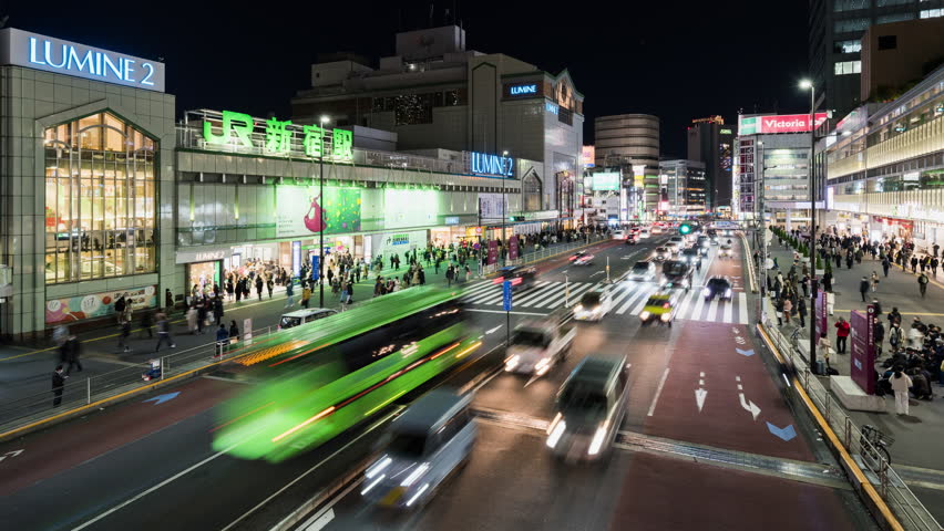 Tokyo, Japan - Dec 2, 2022: Time lapse of car traffic transportation, Japanese people, crowd Asian commuter walk cross road at JR Shinjuku subway train station. Asia transport, urban city night life