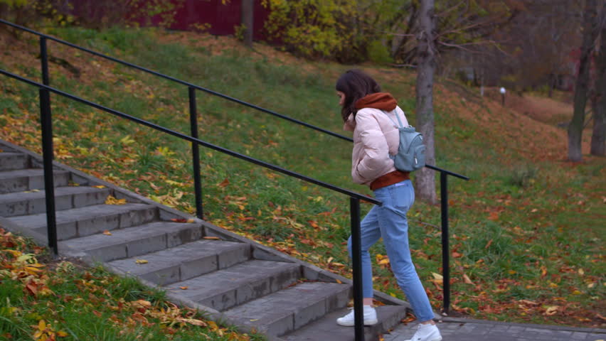 Young woman climbs stairs in park in autumn. Stock footage. Beautiful young woman walks in park in autumn. Woman climbs street stairs in park