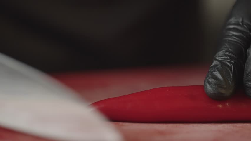 Slicing a chili pepper with a knife close-up slow motion video. The chef prepares food for cooking in the kitchen. High quality 4k footage