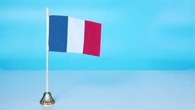 French flag on a blue background. The flag of France flutters in the wind. National flag of France on a rack on a white table. copy space.