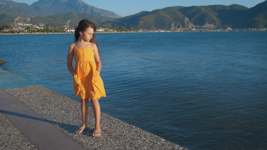Summer with happy child against sea hills. A little girl with long hair stands in the wind against the backdrop of the blue sea.