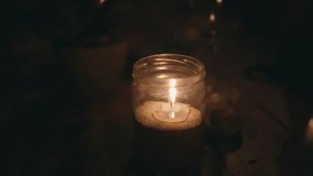 Burning candle in the glass jar on on wooden table in darkness. Soothing cozy video of candle flame fot meditation. Flickering warm flame in the dark