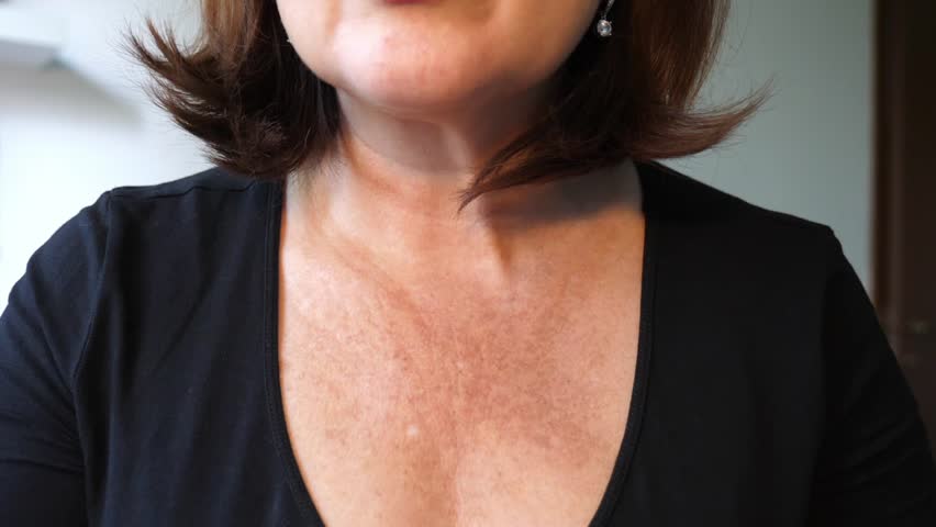 A middle aged woman looks in the mirror at the sun damage on her skin in the neckline and neck area. She has sun spot, wrinkles and discoloration.  | Shutterstock HD Video #1102970689