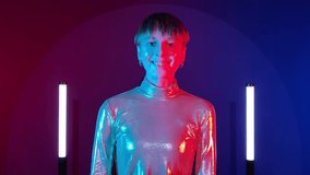 Female android robot makes synthetic smile, learning to express joy in neon illumination indoors. AI concept, sci-fi, future. Young adult woman in futuristic sparkling costume art colorful lighting - Powered by Shutterstock - Get 15% off with code: PIKWIZARD15
