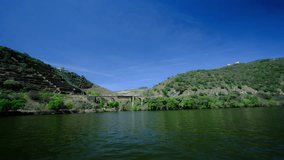 A sunny river cruise, with beautiful blue skies. the river is calm and peaceful, and by the river bank, an old bridge is visible. a 4K video clip, Douro river, Portugal.