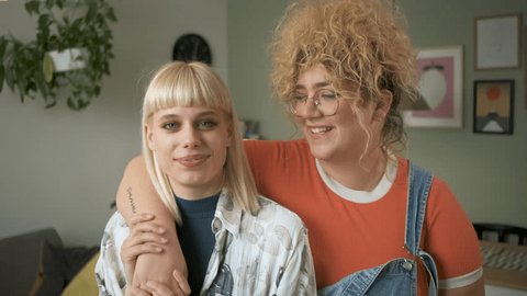 Portrait of a smiling lesbian couple standing in a room, embracing each other and looking at the camera. 库存视频