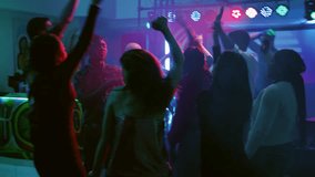 Young adults dancing on electronic music, having fun together with DJ on stage. Cheerful men and women jumping on dance floor under disco lights, enjoying dance party. Handheld shot. - Powered by Shutterstock - Get 15% off with code: PIKWIZARD15