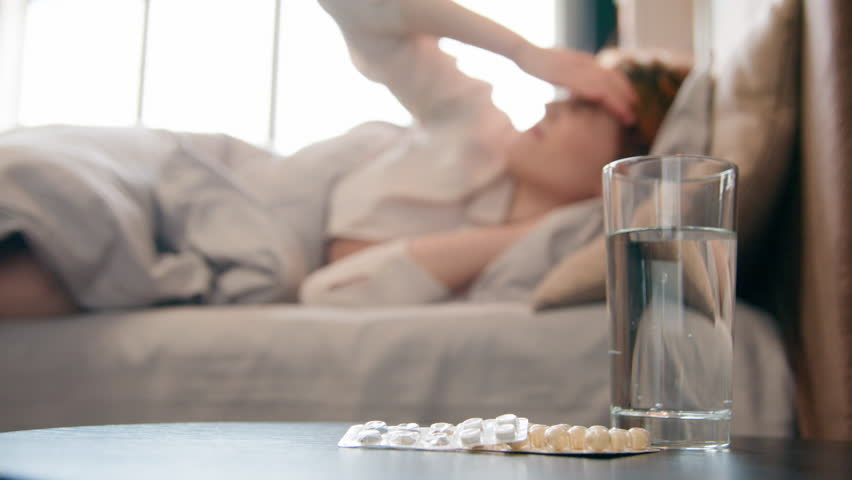 Glass of water and cure drugs on table in bedroom blurry sick woman suffering from headache in bed morning lady painful head migraine fever hangover pain flue coronavirus girl take pills painkiller Royalty-Free Stock Footage #1102976897