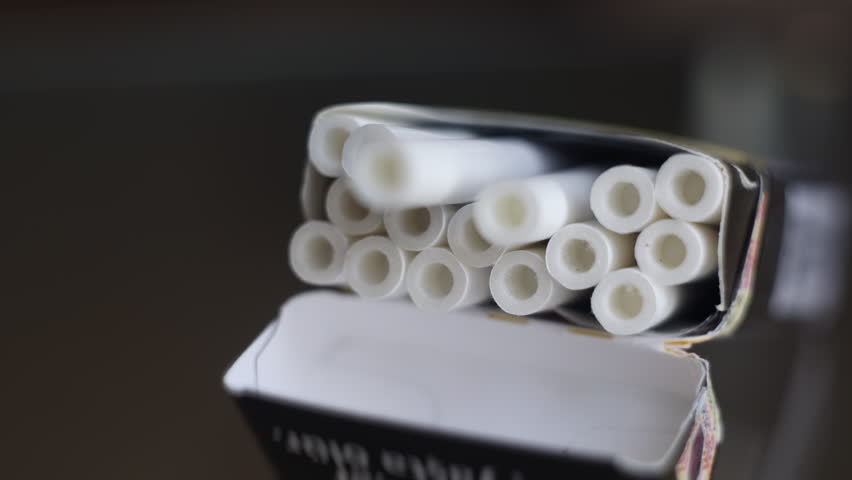 A hand takes a cigarette from an open pack on the table. nicotine addiction, a bad habit. heart disease and lung cancer, death