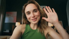 Modern blogger waving hand indoors camera view. Positive girl greeting bestie making hello gesture at room portrait. Smiling woman video calling device started virtual conference at home closeup  - Powered by Shutterstock - Get 15% off with code: PIKWIZARD15