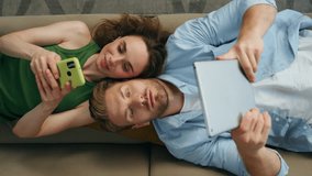 Closeup chilling duet laying sofa at home. Involved couple using gadgets resting together at living room top view. Bearded focused man watching tablet. Relaxed woman browsing mobile phone at apartment - Powered by Shutterstock - Get 15% off with code: PIKWIZARD15