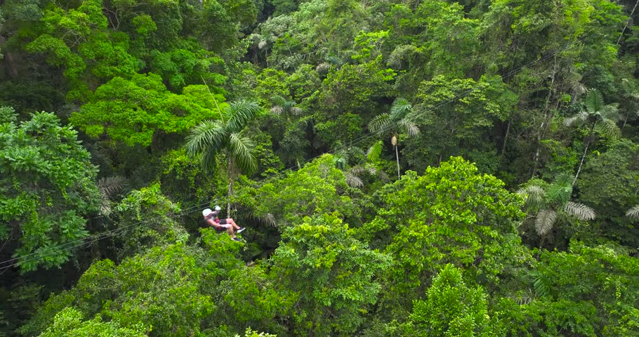 A person coming down from a mountain to the valley on a suspended zipline, surrounded by lush vegetation. Aerial drone view, forward movement.
 Royalty-Free Stock Footage #1102989943