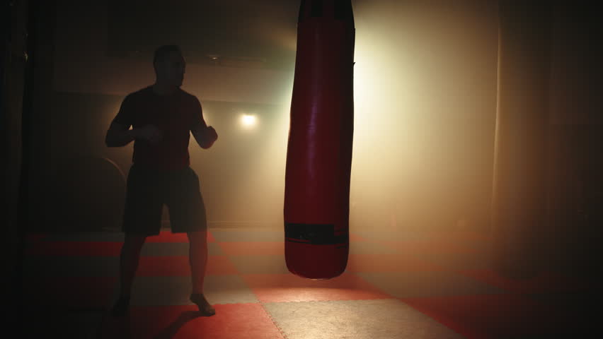 Silhouette of Man Kick boxing against the bag in the gym 