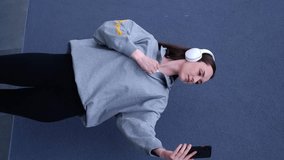 Confident smiling girl in headphones taking selfie on mobile phone isolated on gray background.Blogger lifestyle.Weared in a gray blouse and black skinny, vertical video
