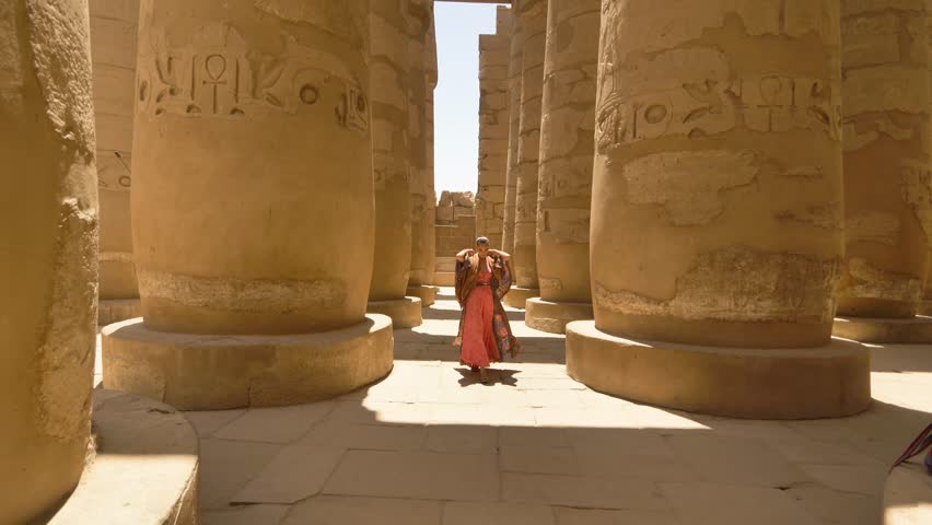 EGYPT - CIRCA 2022 - A woman puts on her hood on as she walks through the columns of Egypt's Karnak Temple Complex. Royalty-Free Stock Footage #1102996179