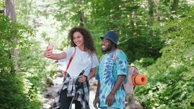 Happy man and woman couple make selfie on smartphone in hike in wild mountains near river. They smiling traveling together, enjoying their trip. Hiking, travel, tourism, summer vacation concept.