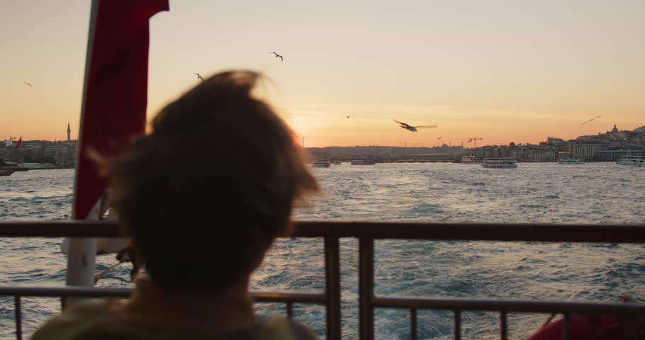 A man sails on a ship past the city during sunset. Sunset in the Bosphorus Strait. Flag of Turkey on the ship. Seagulls fly over the water near the ship during sunset. High quality 4k footage