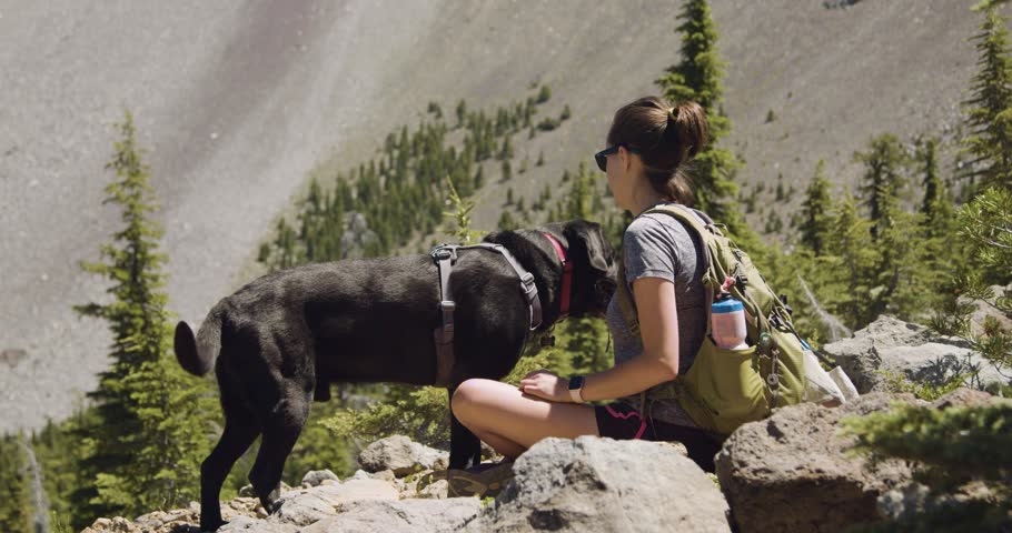 Girl and black lab taking a break on hike with mountain in the background