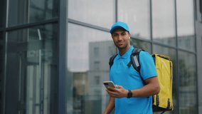 Portrait of the Positive African American Courier in Uniform Standing Near the Business Centre with Bicycle, Using Smartphone and Earphones, Scrolling Customers Orders. Food Delivery - Powered by Shutterstock - Get 15% off with code: PIKWIZARD15