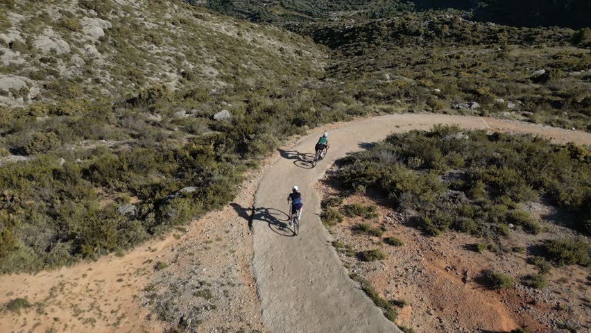Group of gravel cyclists descend a gravel serpentine road in a mountains. Cycling in Spain Costa Blanca concept video. Aerial drone footage in slow motion. Camera revealing breathtaking mountain view.