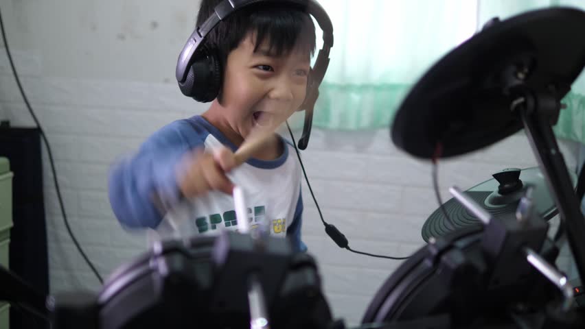 Asian child boy play electronic drum with headphone. Kid beat drumstick in hard rock music at home. Concept of music learning, happy relaxing time, freedom, little kid musician. Royalty-Free Stock Footage #1103012449