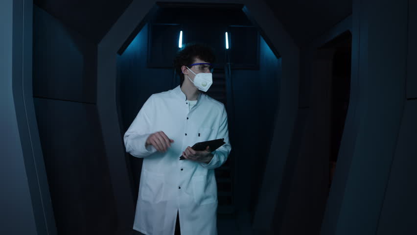 Young medical worker making notes while walking along corridor. Male scientists making laboratory research in protective glasses and mask. High quality 4k footage