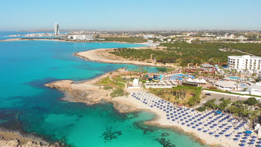 Ayia Napa, Cyprus - 15th april, 2023: aerial fly over Luxury hotel buildings with pools by beach with island greenery panorama. White sand most famous in Cyprus - Nissi beach