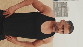 Vertical video, Mature man stretching his neck muscles while standing on the beach in the morning