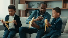African American father dad man teach two children teaching little boys kids sons peel banana show explain how to peeling bananas fruit healthy nutrition development happy family on couch sofa at home - Powered by Shutterstock - Get 15% off with code: PIKWIZARD15