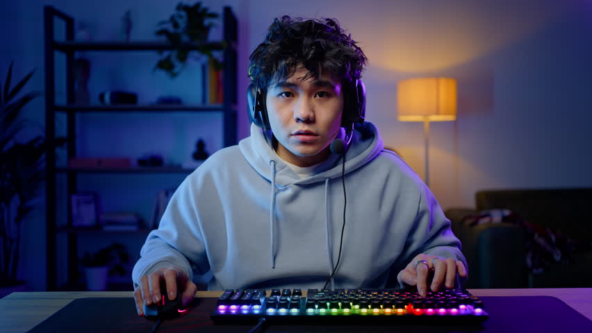 Asian professional gamer man playing online computer game, wearing headset with sad feeling at lose moment. Professional Streamer plays game with computer mouse and keyboard with colorful lights Royalty-Free Stock Footage #1103027353