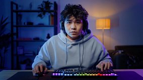 Asian professional gamer man playing online computer game, wearing headset with sad feeling at lose moment. Professional Streamer plays game with computer mouse and keyboard with colorful lights