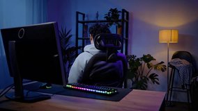 Young Asian man, professional gamer putting on audio headset and starting playing online virtual video games on computer, with inspiration at night time. People. Technology. Gambling. Cyberspace.