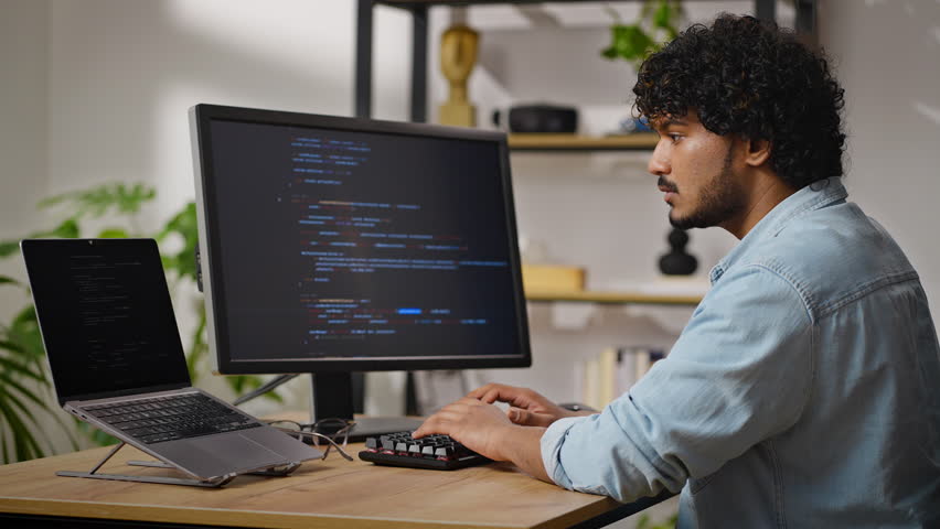 Young Hindus programmer works on computer sitting at desk in cozy apartment. Proficient male with kinky hair types and corrects data carefully - Powered by Shutterstock - Get 15% off with code: PIKWIZARD15