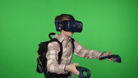 A boy using virtual reality glasses with controllers, playing video games in a studio on a green background. Chroma key.