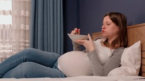 Video of pregnant woman eating a bowl of fresh fruits lying in bed. Leisure activity for pregnant.