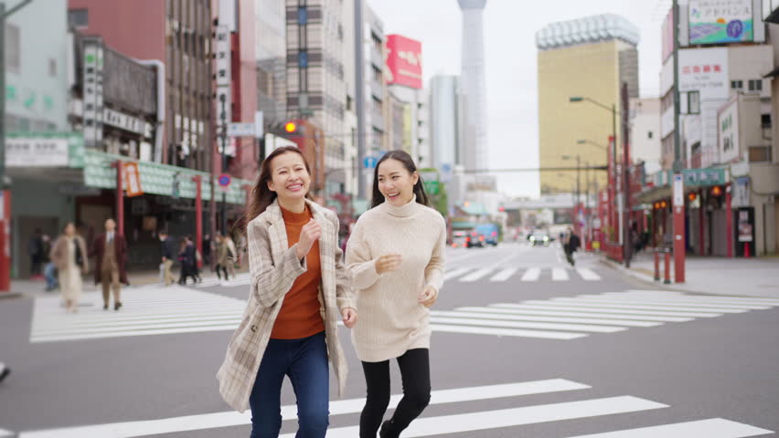 Asian woman friends crossing street crosswalk with crowd of people during travel together at Asakusa, Tokyo, Japan in autumn. Attractive girl enjoy urban outdoor lifestyle travel on holiday vacation. Royalty-Free Stock Footage #1103032359