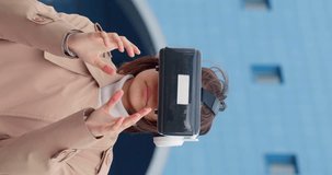 Vertical 4k video of a teenage girl wearing VR glasses, immersed in a virtual world, while gesturing in front of bustling city skyline. Potential of cutting-edge technology in the heart of the metropo