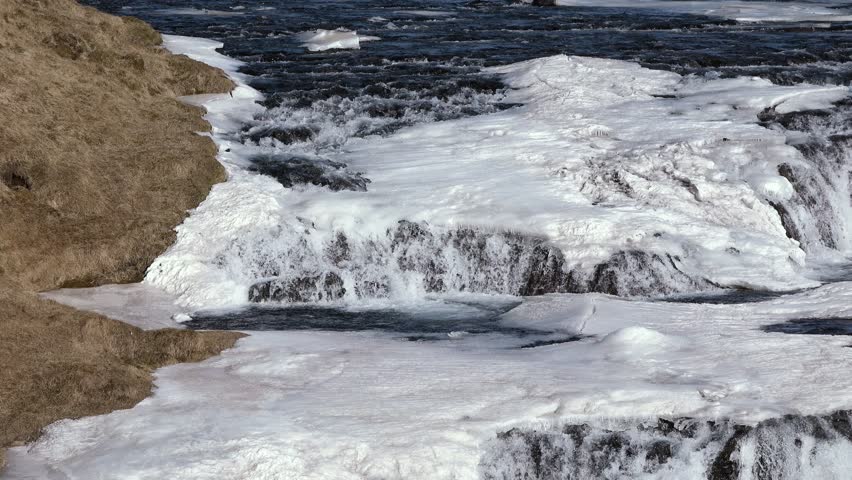 Arctic nature. Waterfall and ice. Winter in Iceland. Icelandic winter landscape. High waterfall and rocks. Snow and ice. A popular place to travel in Iceland.