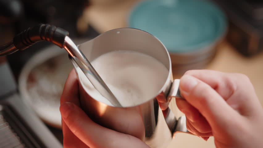 Woman barista heating and foaming fresh milk for making cappuccino or latte coffee hot drink at cafe bar counter. Warm cozy lighting while milk steamer machine working. Close up slow motion | Shutterstock HD Video #1103046759