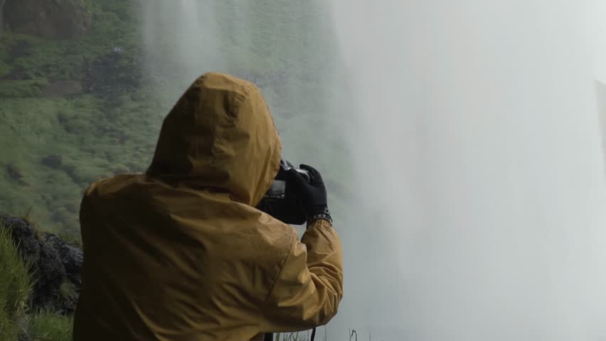 Tourist taking photo with proffesional camera of waterfall Godafoss on Iceland. Man taking picture with camera on travel visiting tourist attractions and landmarks in Icelandic nature 