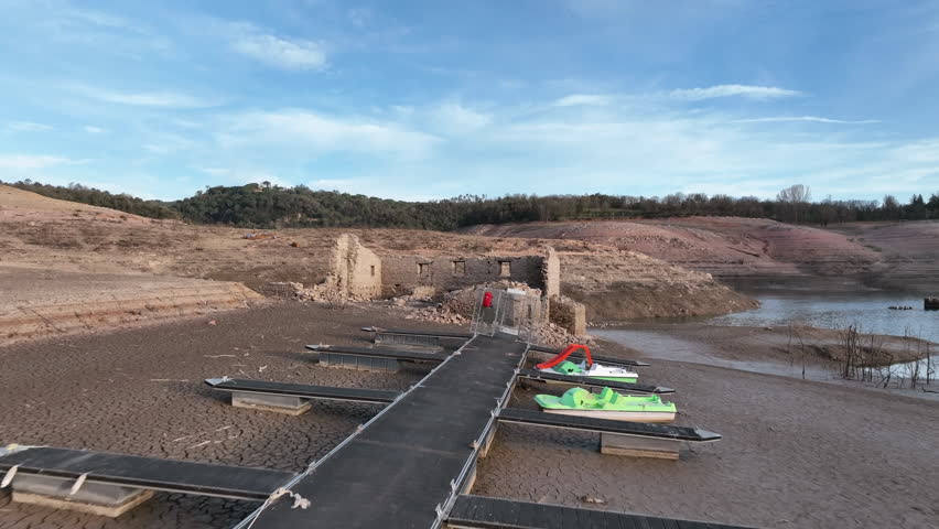 Unusable inaccessible pier and building ruin on dry shores of Sau swamp in Catalonia, Spain. Aerial forward drone low