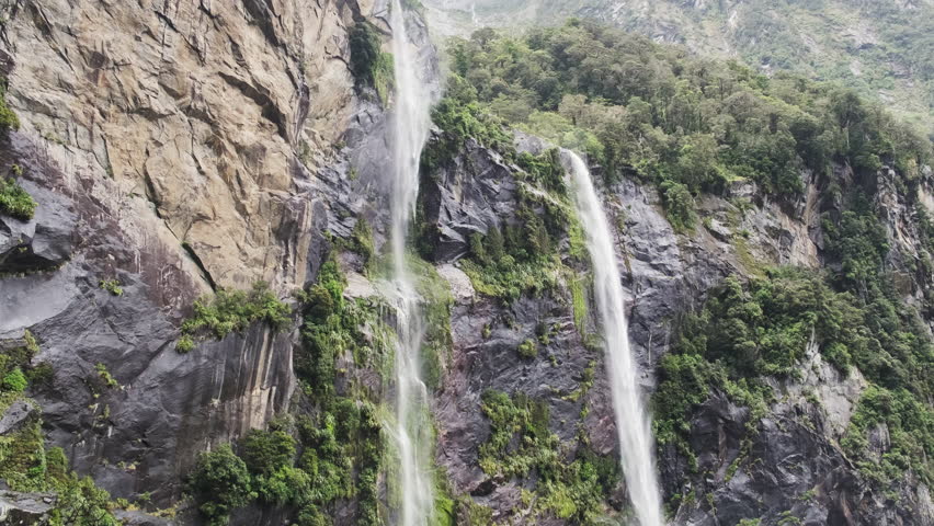 A breathtaking view of waterfalls cascading down from a misty mountain in Milford Sound, New Zealand