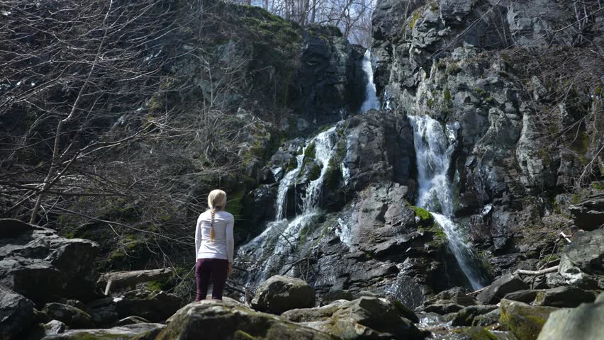 Mature woman with arms outstretched celebrates feeling freedom, success hiking to waterfall in Shenandoah National Park in Blue Ridge mountains of Virginia. 