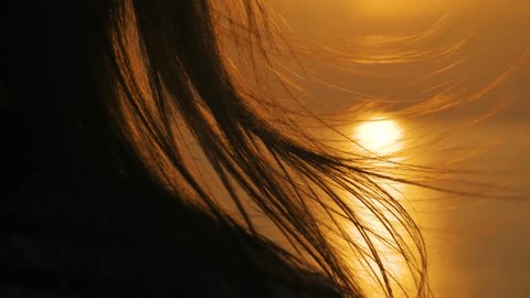 Slow motion: hair of woman is fluttering in the wind against warm sunset sky with sun lens flares, close up. Abstract, freedom and summer concept Stock-video