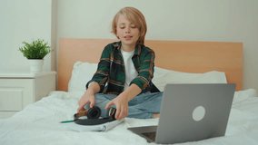 Teenage child boy using laptop and headphones. Child looking online video course lesson in bed. Chat video conference Schoolboy studying doing homework. E-learning, remote educational classes