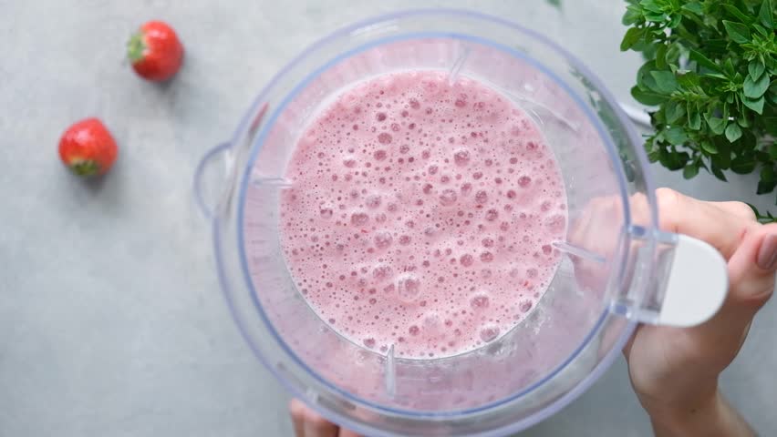 Thick strawberry smoothie or vegan milkshake mixing in a blender. Top view. Cooking process